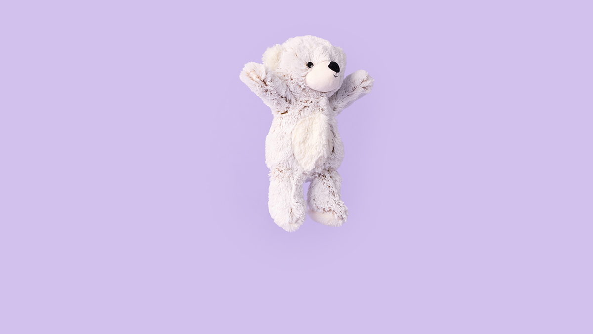 Child sitting on a bench, smiling while tightly hugging a Purple Curly Bear Warmies.