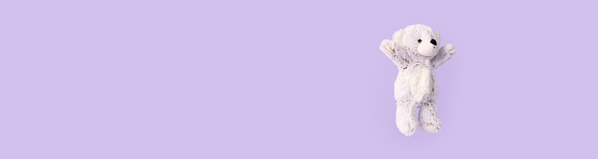 Child sitting on a bench, smiling while tightly hugging a Purple Curly Bear Warmies.