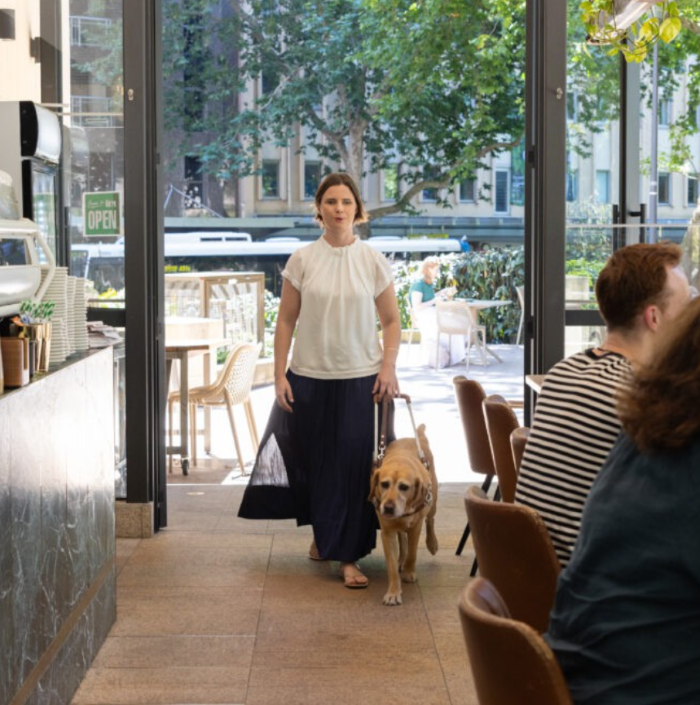 Sarah Hirst walking through a cafe with her yellow Guide Dog.